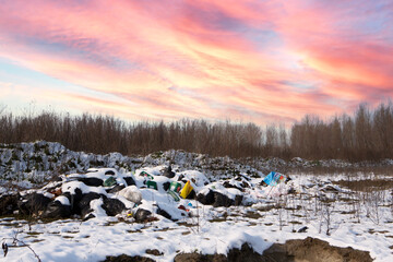 Ecological crisis. Different garbage and trash on snow at beautiful winter forest at colorful sky. Environmental pollution by garbage. Destructive human influence on nature