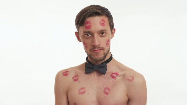 Portrait of one sexy half naked brunette man with wear grey bow tie moves, dancing on white background close up. Romantic concept. Beautiful man kissed by girlfriend with lipstick kiss marks on body.