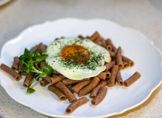 Fried egg with buckwheat noodles  and arugula on white plate