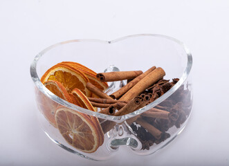 Slices of dried oranges, cinnamon and cardamom in a heart-shaped glass dish