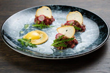 beef tartare with egg, white bread croutons and fresh radish. scrambled eggs with glaze. on a blue marble plate