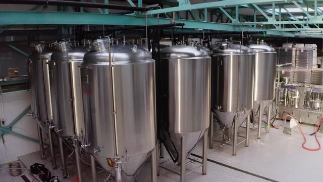 Flying camera view on high volume stainless steel tanks for storing ingredients for production. Equipment of food processing plant.