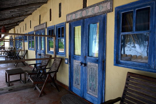 An old hotel on the ocean. An abandoned hotel with carved blue wooden doors and windows. Wooden chairs and a table stand on the terrace of the old hotel. African style hotel on the island Prizon