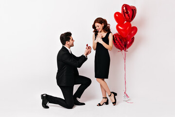 Full length shot of man standing on knee and holding wedding ring. Romantic boy making proposal to girlfriend.