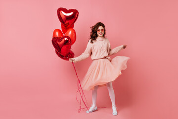Attractive girl with heart shaped balloons dancing and smiling. Full length shot of playful lady celebrating valentine's day.