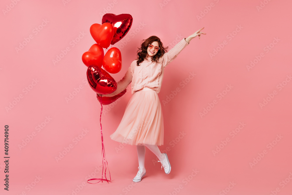 Wall mural Full length shot of blissful woman with red balloons. Studio photo of beautiful ginger girl dancing on pink background.