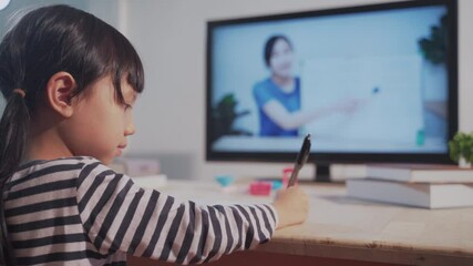 Asian Homeschool student girl us zoom for distance learning online class from teacher at home. Back side of child video call e-learning with tutor in living room, New normal Homeschooling education - Powered by Adobe