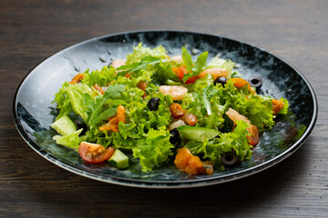 salad of shrimp, fresh cucumber and cherry tomatoes, Chinese cabbage and olives. salad dressed with olive oil. fish salad on a blue marble plate