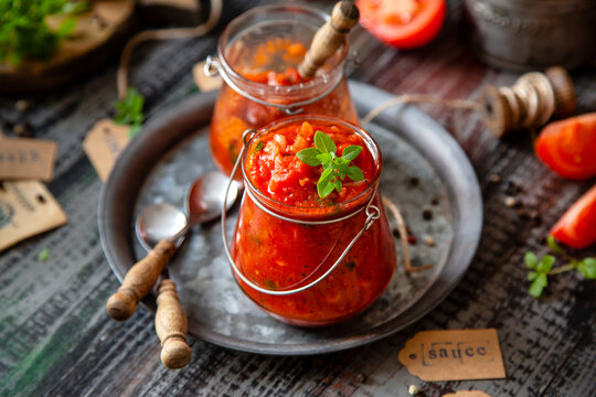 homemade red tomato sauce in glass jar on metal plate on wooden table with basil leaves