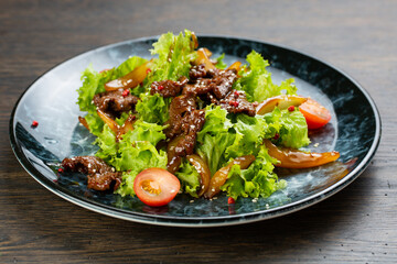 salad of stewed beef, lettuce, pickled peppers and cherry tomatoes. beef salad on a blue marble plate