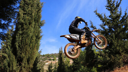 Professional dirt bike motocross rider performing stunts and flying from jump in extreme terrain...