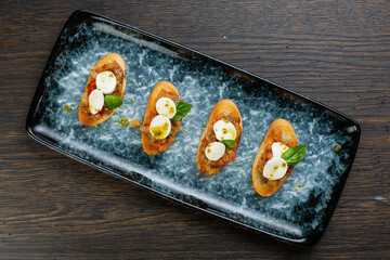 vegetable bruschetta with egg and cheese on white toasted bread. bruschetta on a blue plate. view from above