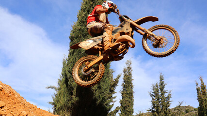 Professional dirt bike motocross rider performing stunts and flying from jump in extreme terrain...
