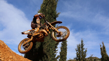Professional dirt bike motocross rider performing stunts and flying from jump in extreme terrain...