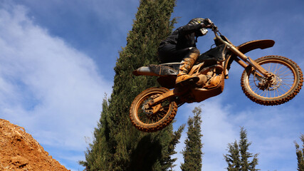 Professional dirt bike motocross rider performing stunts and flying from jump in extreme terrain...