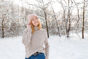 Happy young woman wearing in winter knitted hat and sweater smiling over nature background, Looking at camera and smile. Travel and active life concept. Outdoors