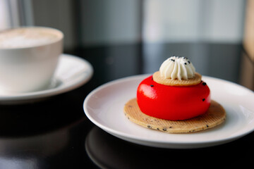 Strawberry cheesecake cake with red icing and cream. Serving on a white plate on a black table. Desserts for womens day. Coffee cup with cappuccino.