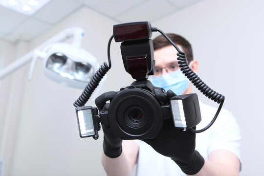 Dentist doctor takes a picture with a camera. A camera with a ring flash in the hands of a doctor. Doctor in a medical mask. Hands in protective black gloves. Modern dental office. Bottom view.