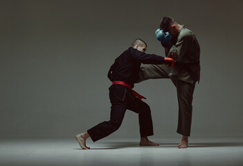 Fighter attacking guy during mixed fight. Males wearing kimono and boxing gloves training martial...