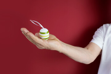 man's hand holds a colored Easter egg with a drawn pattern, red background, concept of Christian traditions, holidays, Spring Festival