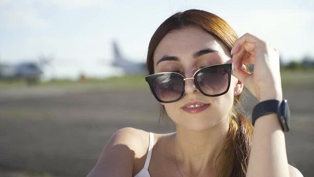 Beautiful Girl Puts Sunglasses on the Background of the Plane
