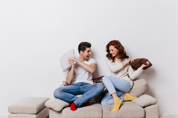 Indoor shot of couple enjoying pillow fight. Laughing family sitting on couch.