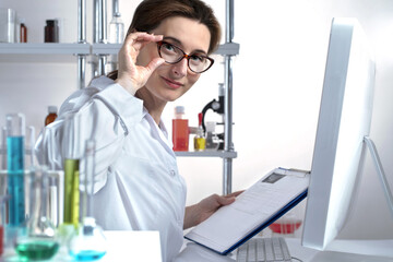 Active woman scientist corrects glasses checking the data in the document paper clip padfolio in a chemical laboratory. Friendly outgoing face. Lifestyle outdoor scene