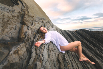 Young caucasian girl wearing only a white shirt on a rocky beach