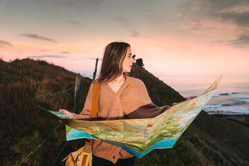 Young caucasian woman looking a map on a natural park next to the coast