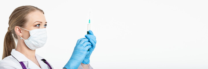 Young nurse in a mask dials the vaccine into a syringe while sitting in a hospital next to a...