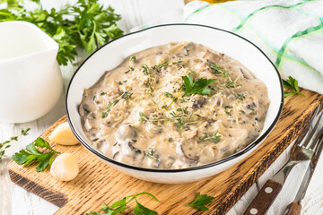 Champignons in cream sauce with herbs and cheese at white table.