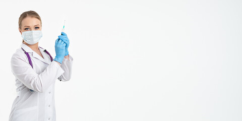 A young nurse in a mask and white coat holds a syringe with a needle for injections, flu shots, covid. The concept of vaccination and protection against influenza, from a pandemic. copy space. banner