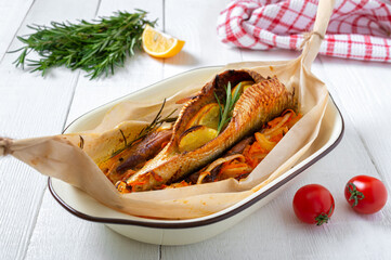 Whole fish baked with vegetables, herbs and orange on a white wooden background.