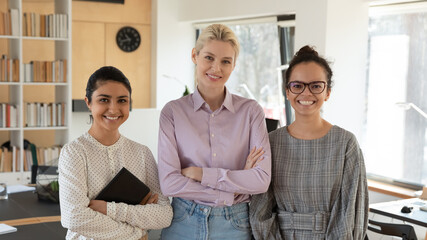 Obraz premium Group portrait of happy international team of female students or interns. Young millennial employees looking at camera and smiling. Diverse business colleagues posing together in office