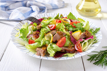Diet salad with magre duck breast, fresh herbs, vegetables and mustard sauce on a light wood background.