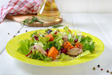 Dietary salad with roast turkey, pumpkin and green lettuce on a white wooden background.