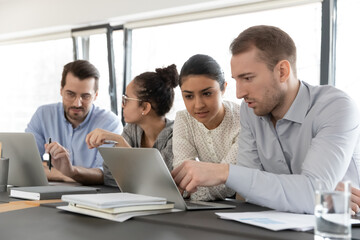 Team members discussing project at shared laptop in office. Millennial business colleagues working at computer together. Indian female coach training intern. Internship, teamwork concept