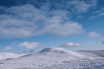 Fototapeta na wymiar Snow covered hill peak under blue sky with fluffy clouds