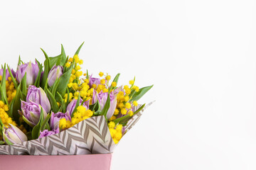 Bouquet of lilac tulips and yellow mimosas in pink box on white background, copy space, side view. March 8, February 14, birthday, Valentine's, Mother's, Women's day celebration, spring concept