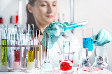 laboratory equipment, supplies, jars, bottles, cylinders, beakers, graduate, test-mixer, medicine-glass. Scientist pouring liquid into beakers in a chemical laboratory in defocus.
