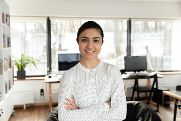 Confident Indian millennial businesswoman posing with hands folded in office. Head shot portrait of...