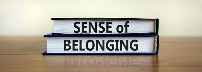 Sense of belonging symbol. Books with words 'sense of belonging' on beautiful wooden table, white...