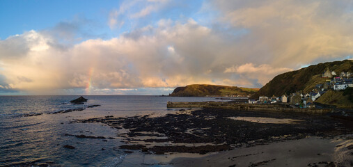 Obraz premium Rainbow appearing from the sea horizon in front of this gorgeous town in north of Scotland by the north coast, this is one of my best aerial shot by a flying drone