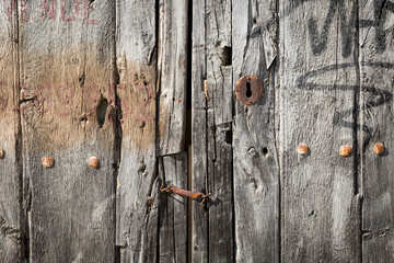 antique gray wooden door with a rusty handle and a lock