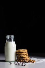 stack of cookies with  a milk bottle and chocolate chips on black background. Front view