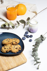 front view of bright breakfast table with cookies, yogurt, blueberry, orange and orange juice. 