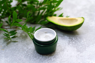 Obraz na płótnie Canvas Bowl of body cream with avocado on grey background. Jar of cosmetic cream, leaves and avocado