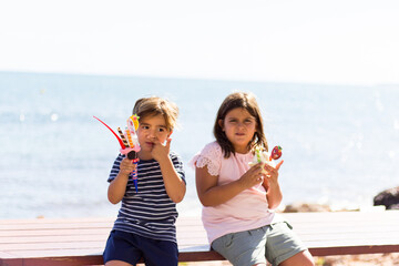 children sitting on a bench, eating ice cream, with the sea in the background