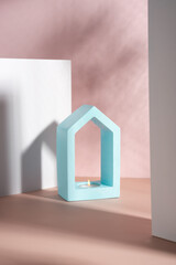 Creative composition. Still life. Shadows on the wall. Minimalistic house-shaped concrete candlestick blue color with soy wax burning scented little candle