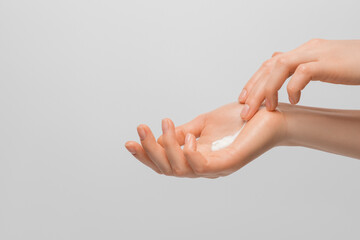 A woman's hands smearing cream on the palm of her hand toward the brush. Groomed hands, natural short nails, on a light background.